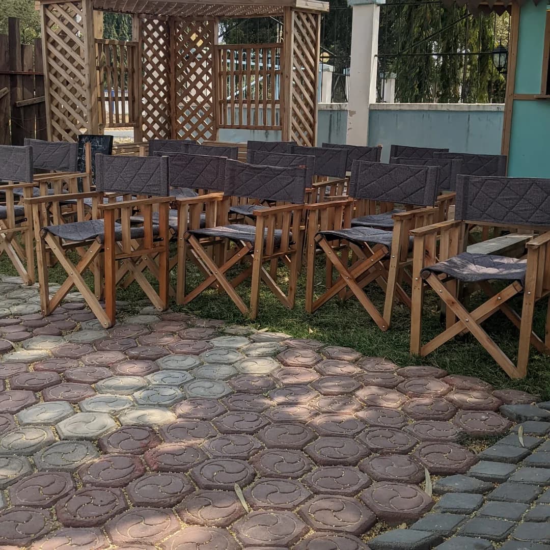 Rows of wooden director's chairs with dark canvas seats on a hexagonal paved patio, in front of a lattice pergola.