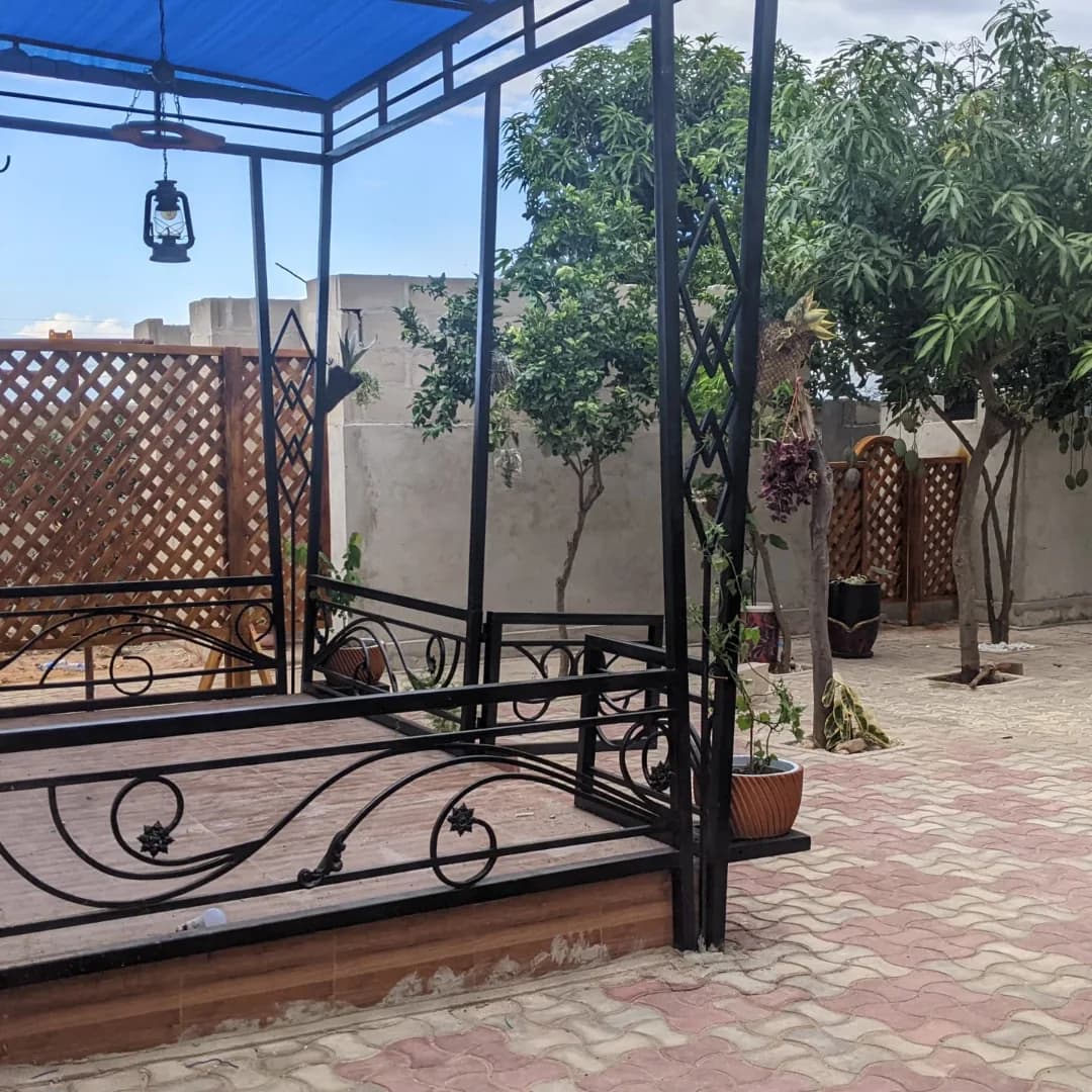 Black wrought-iron garden gazebo with a blue canopy, scrolled iron railings and wood lattice screens.