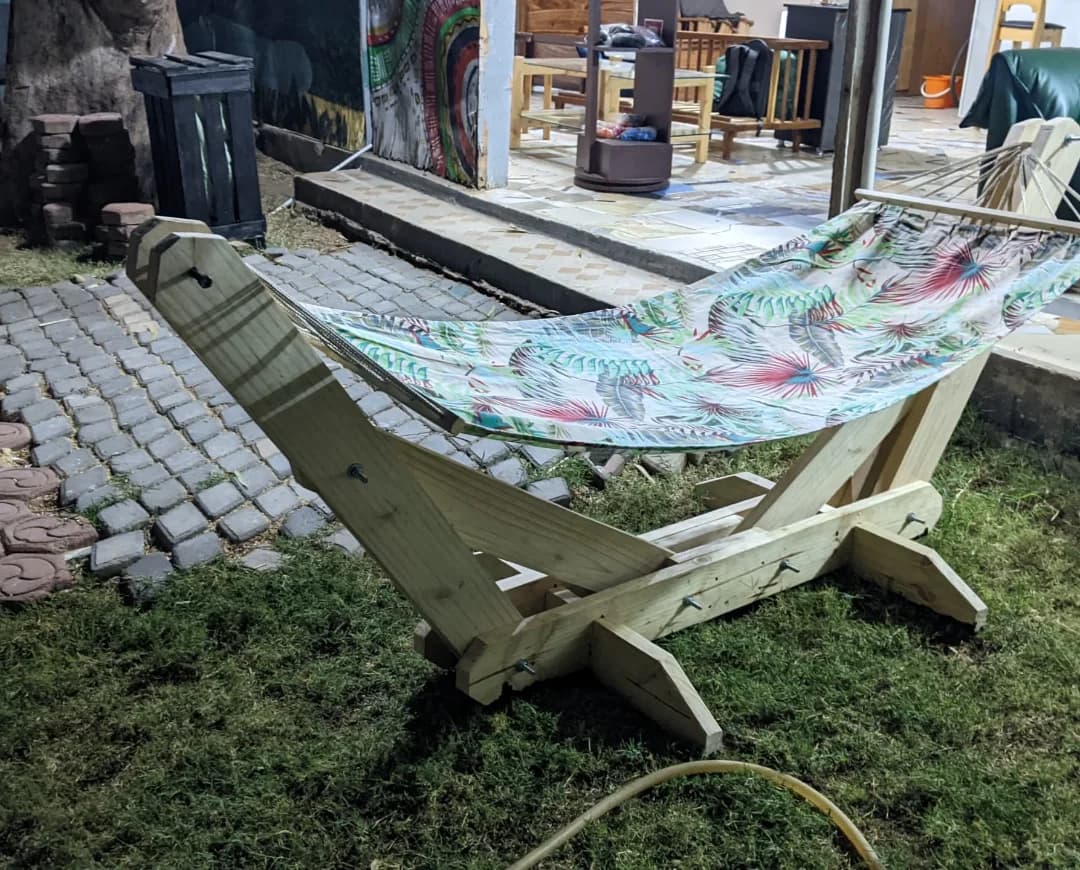 A freestanding wooden hammock stand with a tropical-print fabric hammock, set on grass.